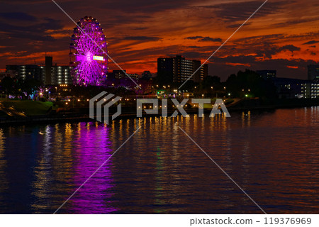 The Ferris wheel at Arakawa Amusement Park and the scenery reflected on the Sumida River. Evening view. Sunset. The Ferris wheel at Arakawa Amusement Park and the scenery reflected on the Sumida River. Evening view. Sunset. 119376969