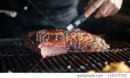 A person uses a thermometer to check the temperature of a perfectly cooked beef brisket on the grill. 119377552