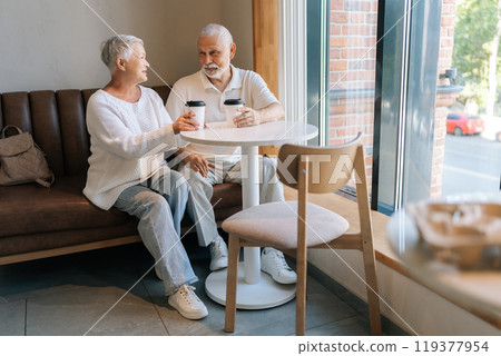 Portrait of elderly couple enjoying coffee in cozy cafe, chatting happily in sunlit room, radiating love and contentment. Happy retirement life filled with leisure, togetherness and cherished moments. 119377954