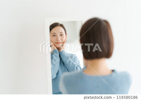 A woman in her 40s smiling in the mirror 119380186