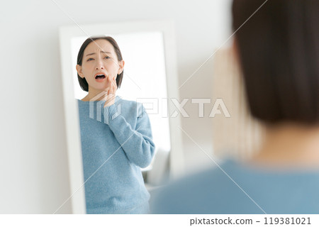 40多歲的女子對著鏡子檢查牙齒 119381021