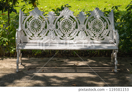Sunlight on backrest surface of Empty ornate antique cast iron bench in a shady area of the quiet park area. 119381153