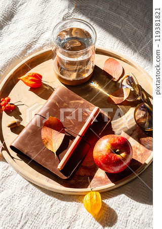 Cozy autumn still life with notebook and fall leaves on wooden tray. 119381821
