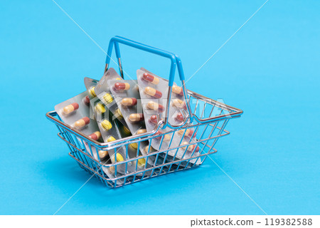 Pills and Capsules in Shopping Basket on Blue Background 119382588