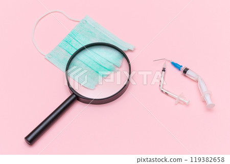 Broken Medical Syringe and Green Torn Medical Face Mask with Magnifying Glass 119382658