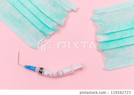 Broken Medical Syringe and Torn Medical Face Mask on the Pink Background Broken Medical Syringe and Torn Medical Face Mask on the Pink Background 119382723
