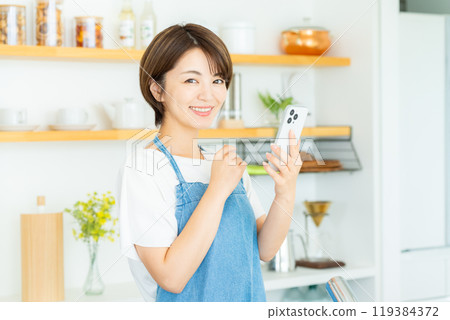 廚房裡拿著智慧型手機的微笑女人 119384372