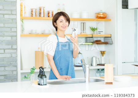 廚房裡拿著智慧型手機的微笑女人 119384373