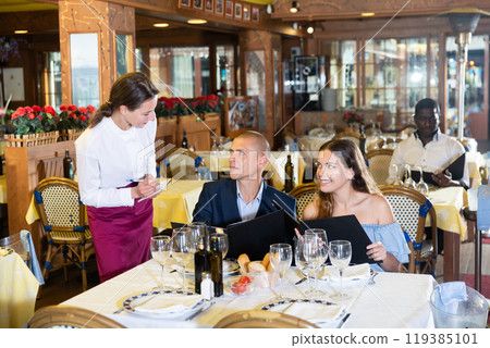 Young positive waitress taking table order from guests 119385101