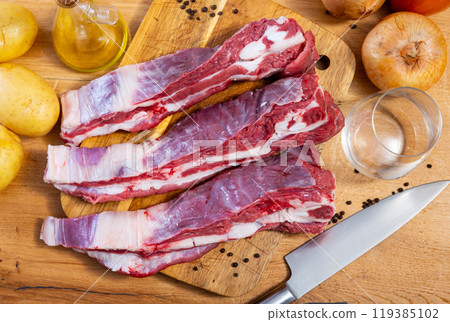Raw beef ribs on board, potato tubers and whole onions 119385102