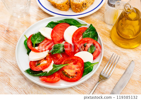 Slices of mozzarella and tomatoes, decorated with basil leaves - traditional Italian salad caprese 119385132