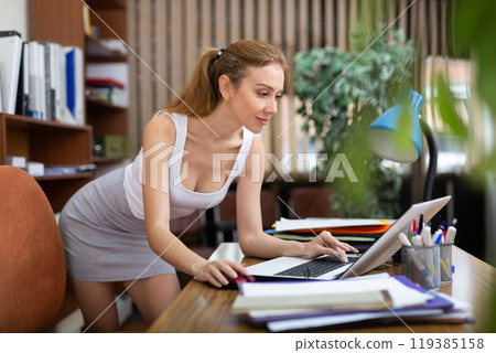Positive young businesswoman working with laptop and papers in office 119385158