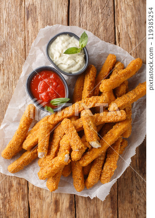 Fried breaded chicken fingers with ketchup and mayo close-up on parchment. Vertical top view 119385254