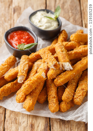 Fried breaded chicken fingers with ketchup and mayo close-up on parchment. Vertical 119385259