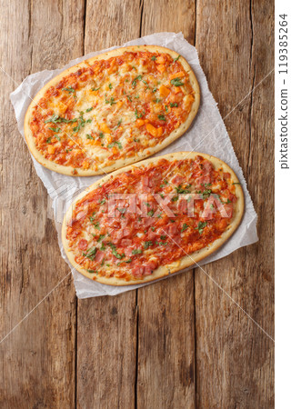 Oval portion pizza of two types three cheeses and cheese with ham close-up on parchment. Vertical top view Oval portion pizza of two types three cheeses and cheese with ham close-up on parchment. Vertical top view 119385264