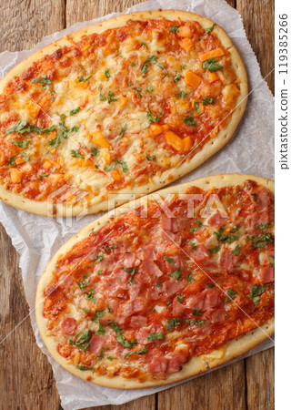 Italian oval pizza focaccia with cheese, ham and tomato sauce close-up on parchment on wooden table. Vertical top view 119385266