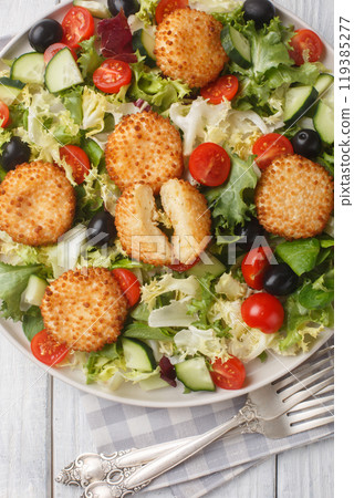 Salad of fried breaded cheese balls, tomatoes, cucumber, olives and lettuce close-up in a plate. Vertical top view Salad of fried breaded cheese balls, tomatoes, cucumber, olives and lettuce close-up in a plate. Vertical top view 119385277