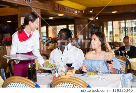 Ordinary female waiter carrying order for visitors in restaurant 119385340