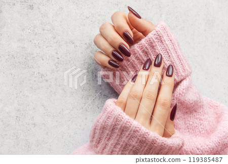 Elegant maroon manicured nails displayed against a soft pink sweater on a textured gray background Elegant maroon manicured nails displayed against a soft pink sweater on a textured gray background 119385487