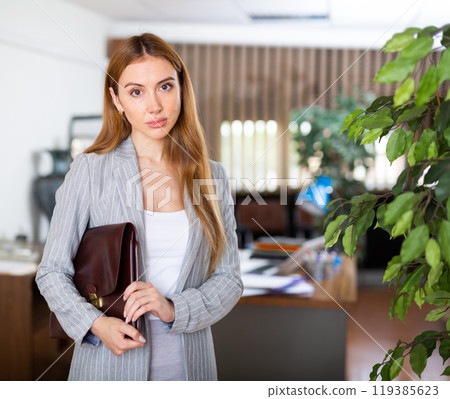 Young confident businesswoman is standing with a folder of documents in a office 119385623