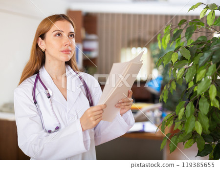 Young female therapist is studying important documents while standing in the office Young female therapist is studying important documents while standing in the office 119385655