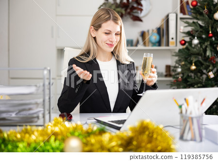 Woman manager with glass of champagne having video call conversation in Christmas decorated office 119385756