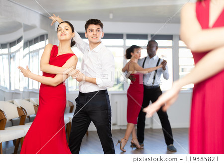 Happy young man and woman in elegant clothes performing ballroom dance in dancing room during celebration or party 119385821