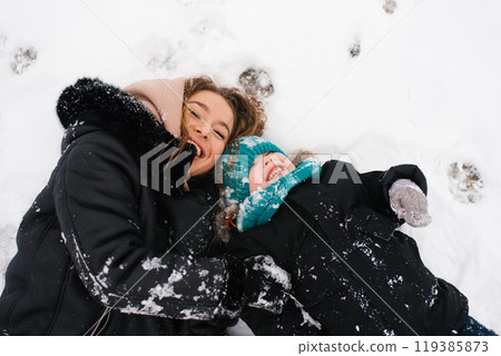 Mother and little son are laying in the snow, both smiling Mother and little son are laying in the snow, both smiling 119385873