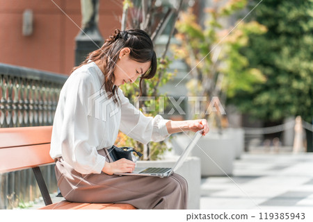 A businesswoman working on a computer on a park bench (urgent, anxious, in trouble, urgent) A businesswoman working on a computer on a park bench (urgent, anxious, in trouble, urgent) 119385943