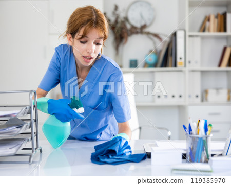 Cleaning lady of cleaning company wipes dust from table in office 119385970