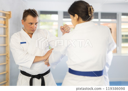 Middle-aged man attendee of karate classes fighting with his opponent in sports hall 119386098