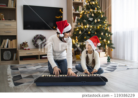 Mother and daughter play piano and sing Christmas songs at home 119386229