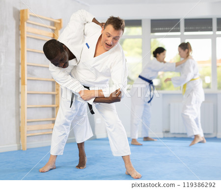 Two males practicing judo together on sports mats under the guidance of trainer 119386292