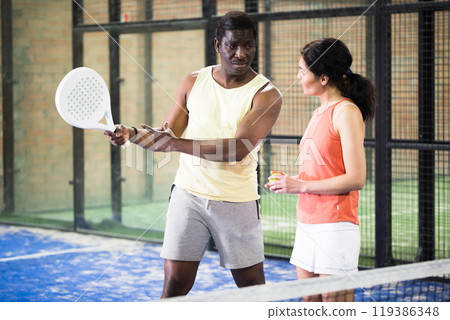 African American padel tennis trainer explaining forehand technique to woman 119386348