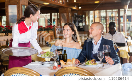 Waitress serving food for couple at restaurant 119386414