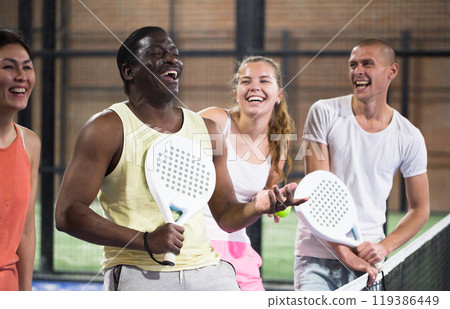 Four smiling men and women with padel rackets posing at court Four smiling men and women with padel rackets posing at court 119386449