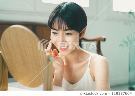 一位女士一邊看著木桌鏡子一邊做皮膚護理 119387604