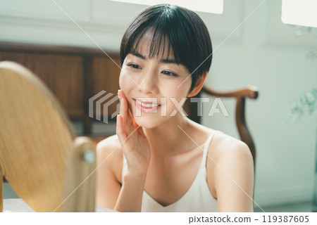 一位女士一邊看著木桌鏡子一邊做皮膚護理 119387605