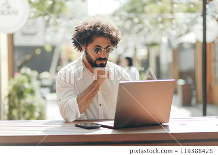 Business portrait, Arabian businessman sitting with laptop computer in outdoors cafe. Freelancer working outdoors Business portrait, Arabian businessman sitting with laptop computer in outdoors cafe. Freelancer working outdoors 119388428