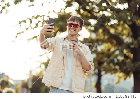 Cheerful man blogger taking selfie on smartphone with take away coffee cup in the morning 119388483