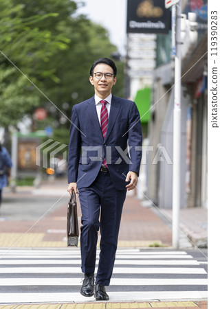 一位中年商人背著商務包在城裡散步。 119390283
