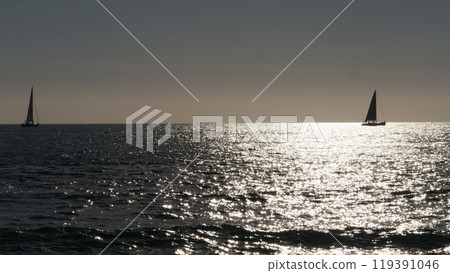Two sailboats sailing away on calm ocean at sunset with sparkling water Two sailboats sailing away on calm ocean at sunset with sparkling water 119391046