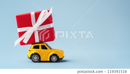 Car toy with red christmas gift box on the roof on blue background Car toy with red christmas gift box on the roof on blue background 119391516