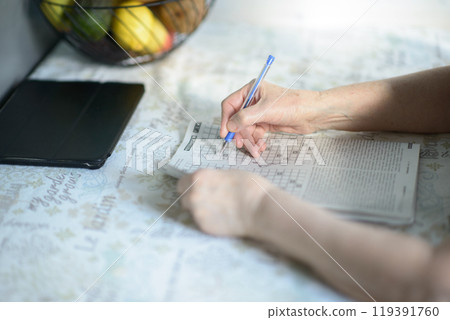 Senior Woman Solving Crossword Puzzle with Tablet and Fruit Bowl in Background Senior Woman Solving Crossword Puzzle with Tablet and Fruit Bowl in Background 119391760