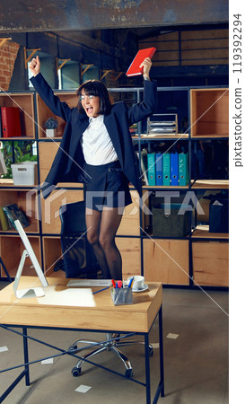 Happy emotional business woman dancing on office chair and celebrating triumph and major personal victory in business. Happy emotional business woman dancing on office chair and celebrating triumph and major personal victory in business. 119392294