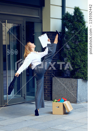 Joy of freedom. Happy young woman in formal wear dancing outside the office, expressing positive emotions after quitting job 119392442
