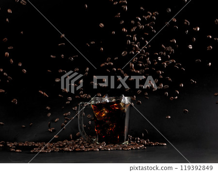 Ice americano Coffee in glass with roasted bean falling. Black background isolated element. Many Coffee Beans fall on Ice cold drink with aroma scent Ice americano Coffee in glass with roasted bean falling. Black background isolated element. Many Coffee Beans fall on Ice cold drink with aroma scent 119392849
