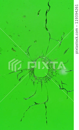 Close-up of gunshot through the glass, shattering against the green background 119394261
