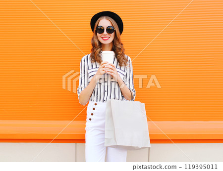 Fashion pretty young smiling woman model with shopping bag holding coffee cup over orange background Fashion pretty young smiling woman model with shopping bag holding coffee cup over orange background 119395011