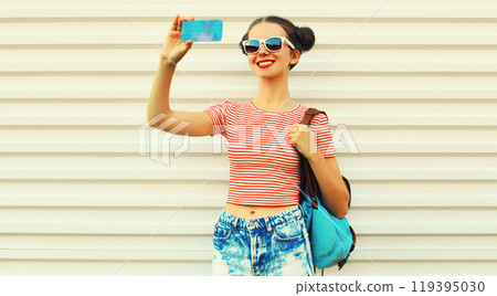 Portrait of happy smiling young woman taking selfie by smartphone with backpack on white background Portrait of happy smiling young woman taking selfie by smartphone with backpack on white background 119395030